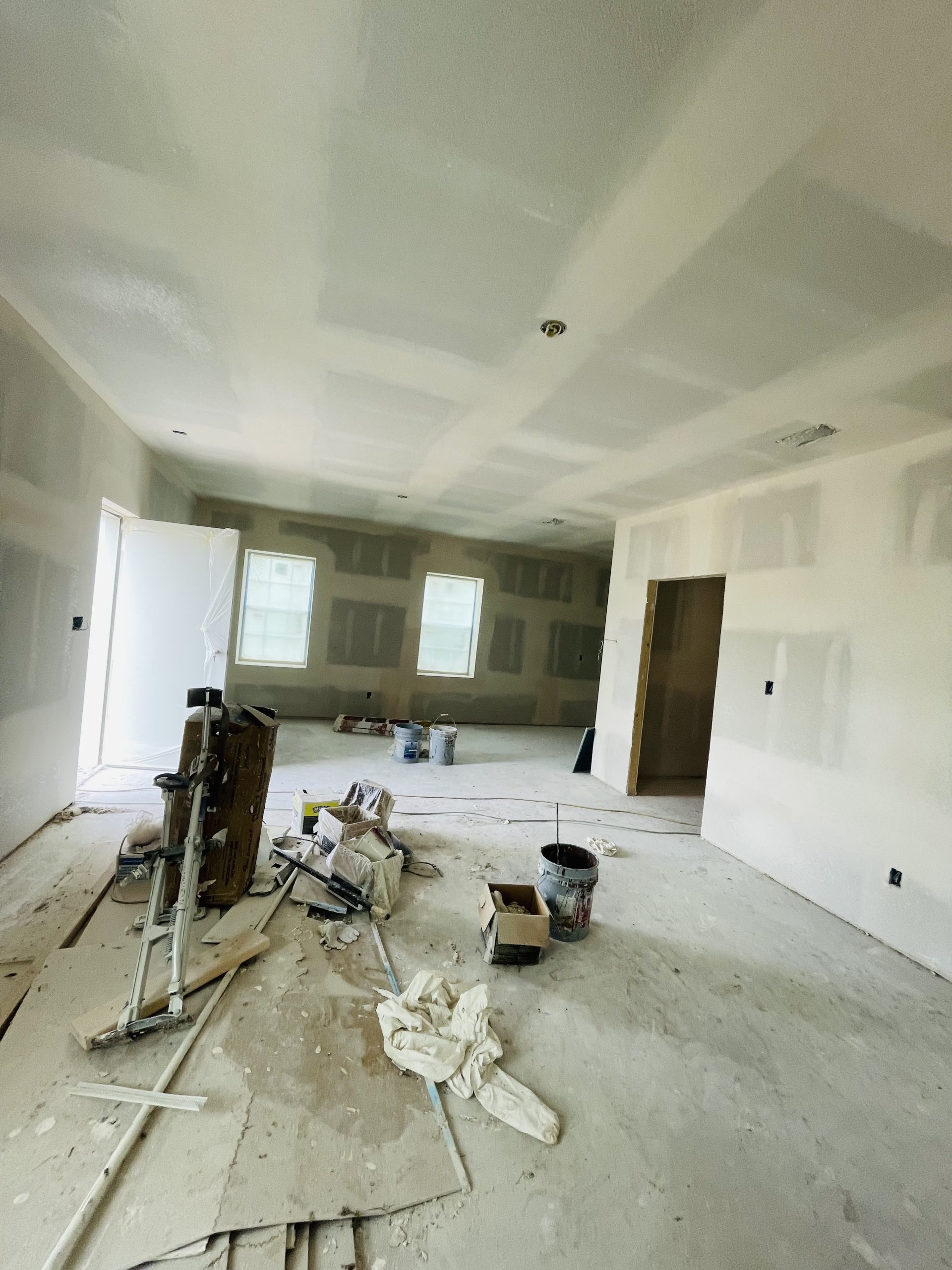 Interior view of a room under construction, with drywall installed and painting equipment scattered around.